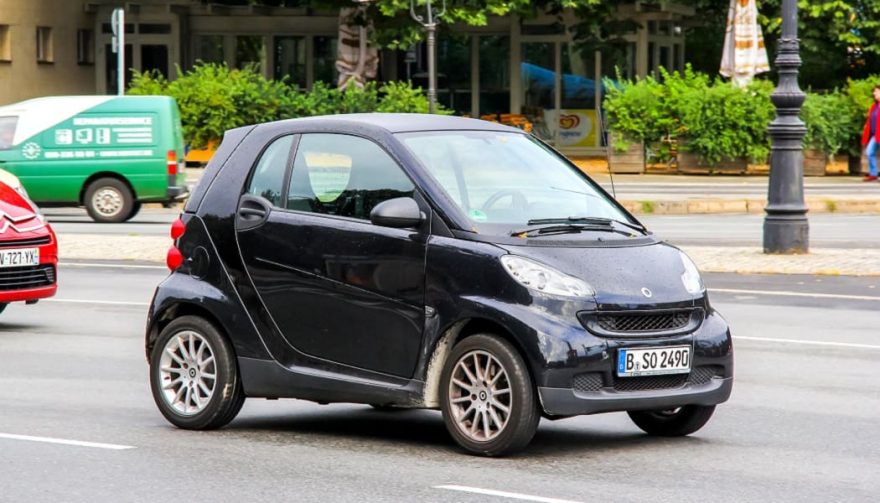 A gas-powered Smart car drives down the street