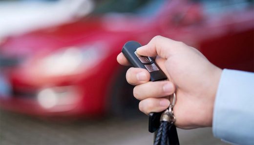 How to rent our your car A person holding a black car key fob in front of a blurred red vehicle.